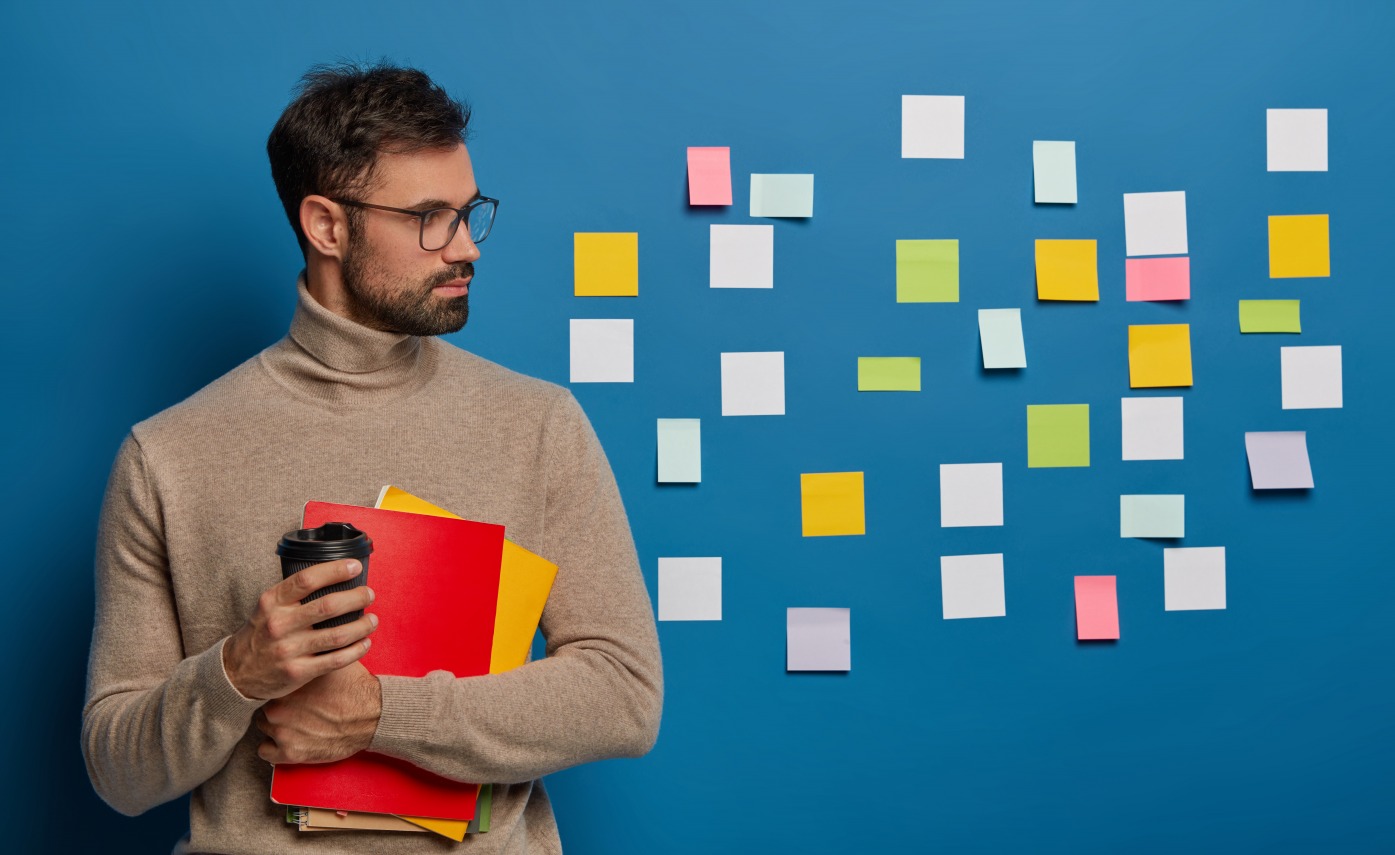 un-homme-non-rase-concentre-prend-du-cafe-se-detourne-sur-un-mur-bleu-avec-des-notes-colorees-adhesives-beaucoup-de-travail-et-de-taches