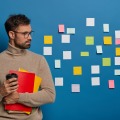 un-homme-non-rase-concentre-prend-du-cafe-se-detourne-sur-un-mur-bleu-avec-des-notes-colorees-adhesives-beaucoup-de-travail-et-de-taches